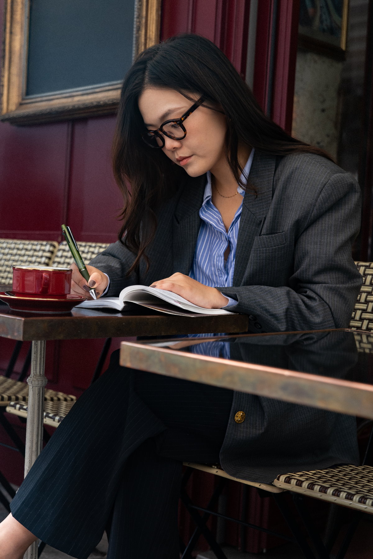 Nina Xu writing at a Paris cafe table, red banquette behind her