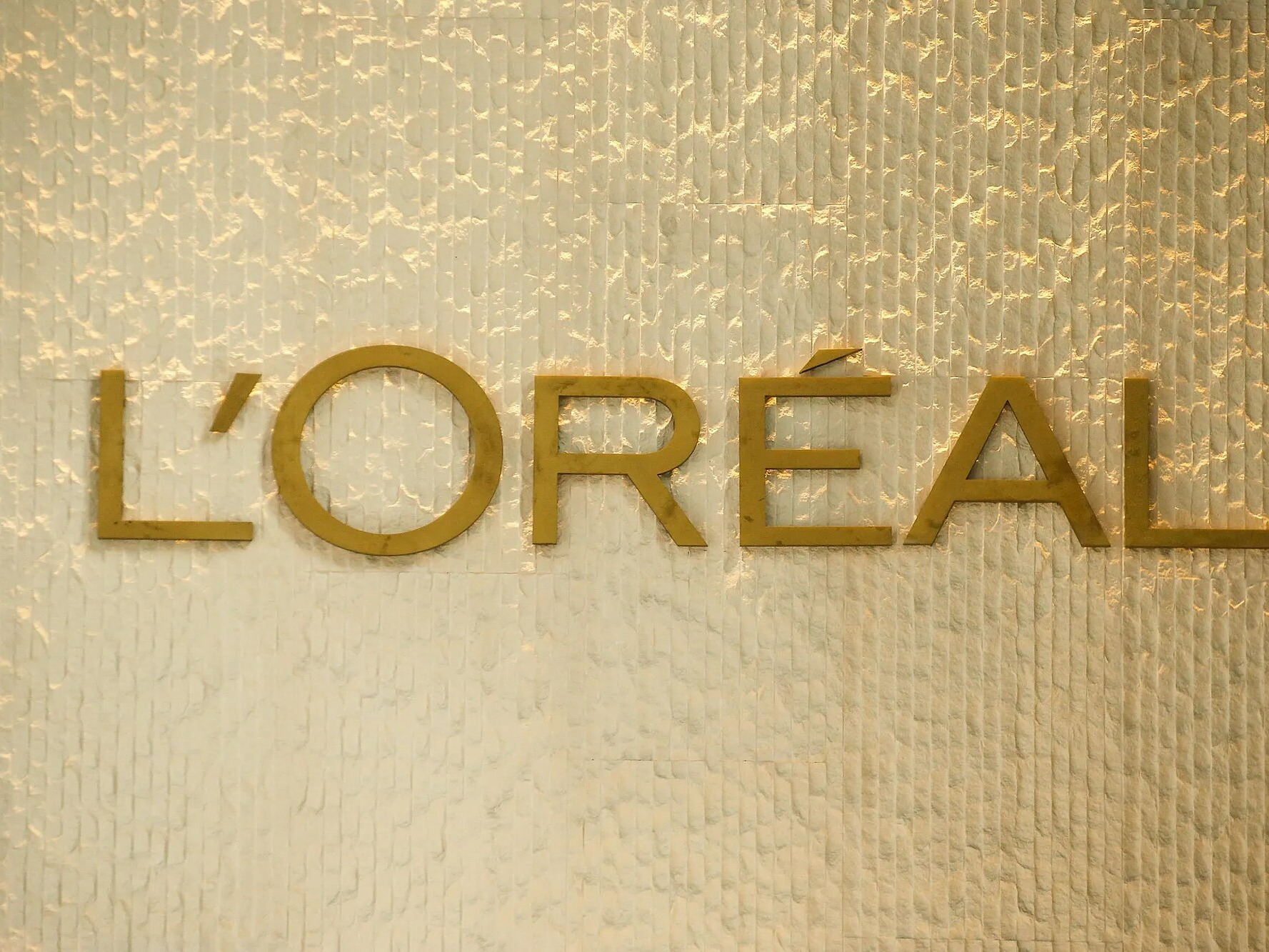 The L&rsquo;Or&eacute;al wordmark in gold on a textured wall